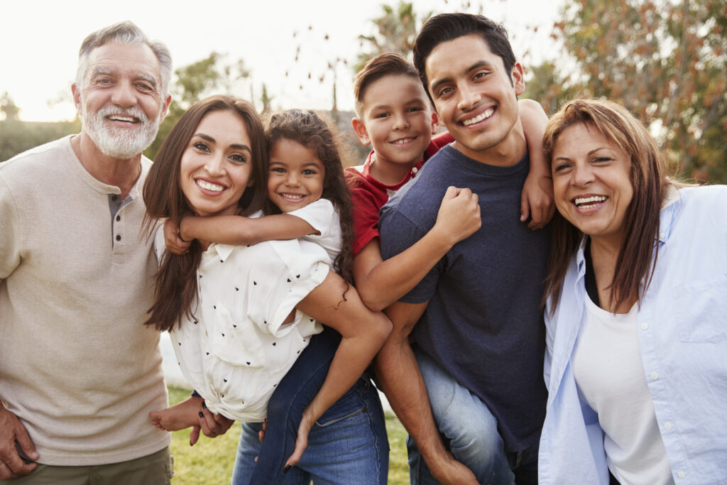 Three generation Hispanic family standing in the park, smiling to camera, selective focus